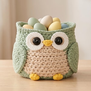 Peut inclure: Un panier en forme de hibou crocheté, vert et beige, rempli d'œufs aux couleurs pastel. Le hibou a de grands yeux ronds avec des pupilles noires et des détails blancs et beiges. Un objet décoratif charmant.