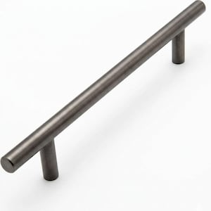 May include: A single, dark gray cabinet pull handle with a cylindrical bar and two cylindrical posts. The handle is made of metal and has a matte finish. The hardware is designed for use on cabinets and drawers.