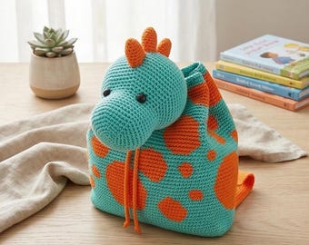 May include: A turquoise and orange crochet drawstring backpack shaped like a dinosaur. The bag features a rounded dinosaur head with black bead eyes, orange spikes on top, and a body patterned with orange spots. Two orange drawstrings hang down.