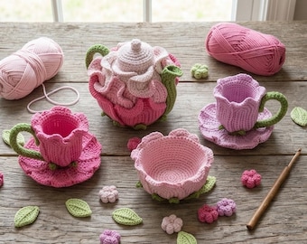 May include: A handmade crochet tea set in shades of pink and green, including a teapot, two teacups with saucers, and a small bowl. The set is flower-shaped, with green accents on the handles and leaves. Yarn and crochet hook are also visible.