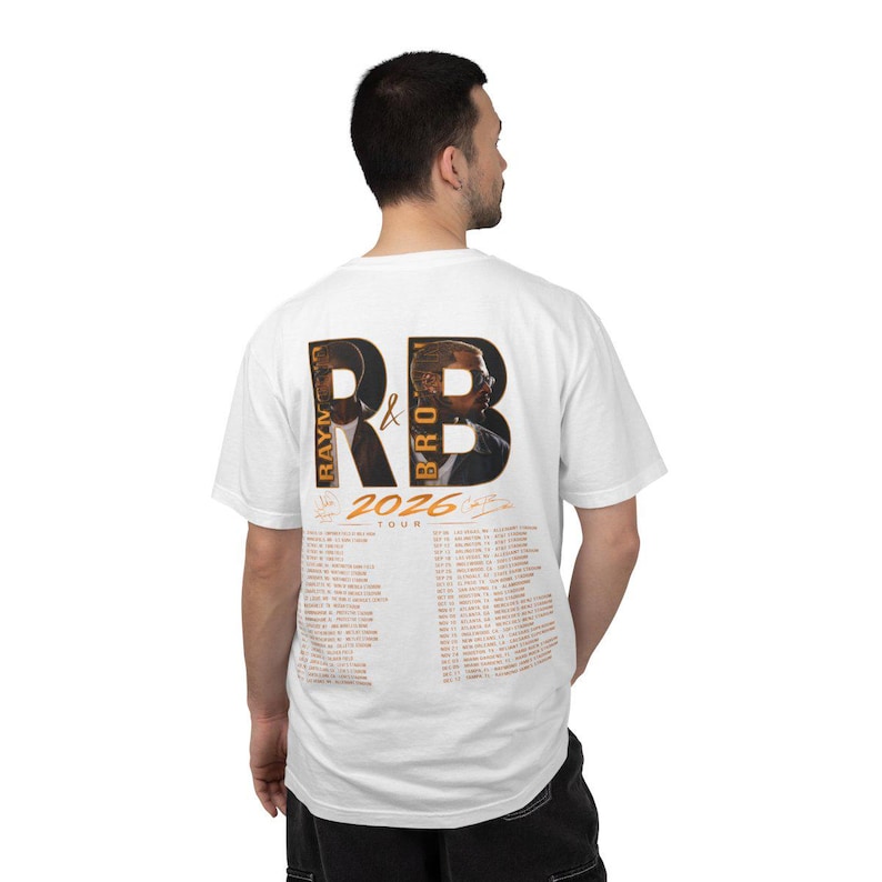 May include: A white short-sleeve t-shirt featuring a graphic on the back with the large letters RB, portraits of two individuals, the text RAYM & BRO, 2026 TOUR, and a list of tour dates and locations printed in orange and black ink.