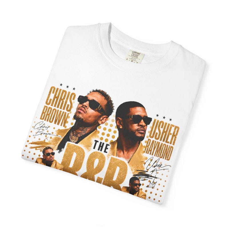 May include: A white t-shirt featuring a graphic print of Chris Brown and Usher Raymond. The design includes gold text reading CHRIS BROWN and USHER RAYMOND, the words THE R&B, and smaller images of the artists. The shirt has a crew neck collar.