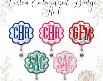 Könnte beinhalten: Fünf gewellte Ausweishalter mit individueller Stickerei auf floralem Stoffhintergrund und dreibuchstabigen Monogrammen in blauem, rosa, rotem und grünem Garn. Der Text Custom Embroidered Badge Reel steht oben.
