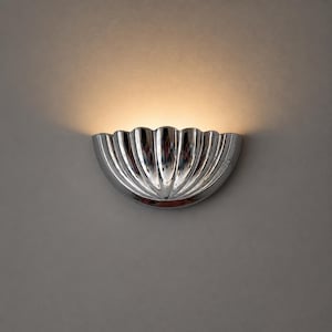 May include: A polished chrome wall sconce with a scalloped, shell-like design. The light fixture is mounted on a gray wall, with a warm glow emanating from the top of the sconce.