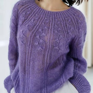 May include: A long-sleeved, fuzzy, purple knit sweater featuring a round neckline and a vertical ribbed pattern with integrated braided cable details radiating from the collar down the front of the garment, crafted with a semi-sheer, loose knit.