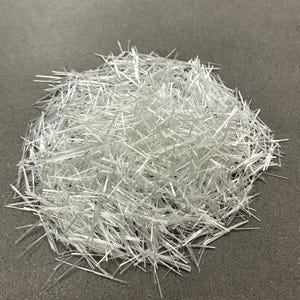 Könnte beinhalten: Ein Haufen durchscheinender, weißer Glasfasern. Die Fasern sind dünn, gerade und scheinen zufällig auf einer grauen Oberfläche angeordnet zu sein. Die Fasern sind dicht gepackt und erzeugen ein strukturiertes Aussehen.