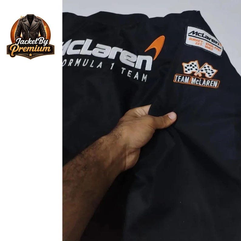 May include: Black McLaren Formula 1 Team jacket with white and orange accents. Features the McLaren logo and text, along with a Team McLaren patch. The jacket has a classic design.