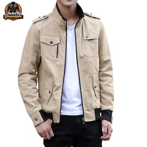 May include: A beige jacket with a black collar and cuffs. It has a zip-up front, several pockets, and button details on the shoulders and pockets. The logo "Jacket By Premium" is visible in the top left corner.