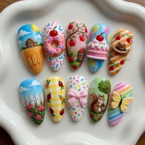 May include: Ten painted fingernails with diverse designs. The designs feature a farm scene, a donut, apples on a tree, a cake, a cowboy hat, a fence with roses, ladybirds on a checked pattern, a bow, a squirrel, and a butterfly.