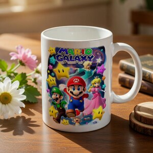 May include: White ceramic mug featuring a colorful graphic of Mario, Luigi, Princess Peach, and other characters from the Mario Galaxy game. The mug has a large handle and the words "Mario Galaxy" are displayed on the front.