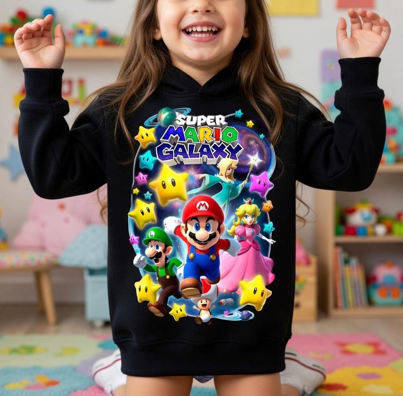 May include: Black hooded sweatshirt featuring a colorful graphic of Mario, Luigi, Princess Peach, and other characters from the Super Mario Galaxy video game. The design includes stars and the game's logo.