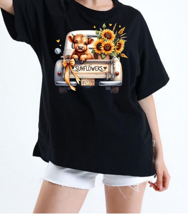 Pu&ograve; includere: T-shirt nera con una grafica di un cassone di camion vintage bianco pieno di girasoli e un vitello. Il cassone del camion ha la scritta "SUNFLOWERS" e una targa. Un fiocco giallo &egrave; legato al camion.
