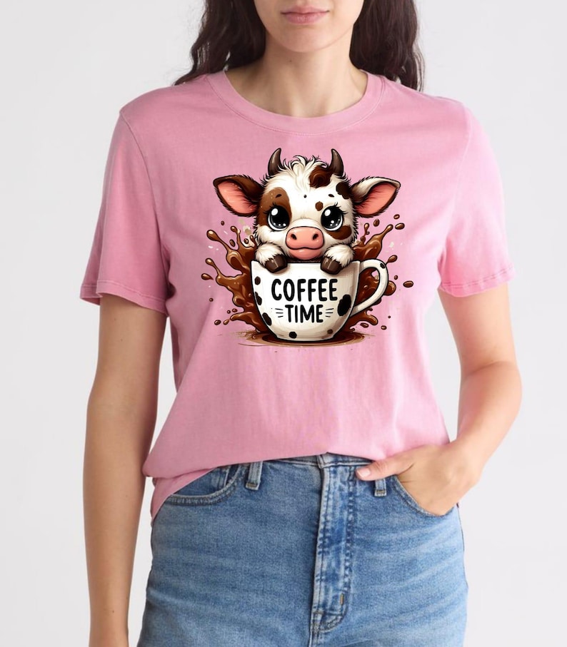 Pu&ograve; includere: T-shirt rosa con un disegno di mucca dei cartoni animati. La mucca, con macchie marroni e bianche, &egrave; in una tazza di caff&egrave; con la scritta "COFFEE TIME". Il disegno include uno schizzo di liquido marrone intorno alla tazza.