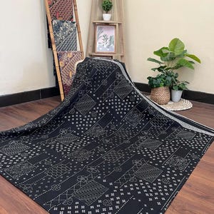 May include: A black fabric textile featuring a white geometric and floral pattern with a grid-like layout. The material displays various repeating motifs including small flowers, cross-hatching, and wavy lines, finished with a white border edge.