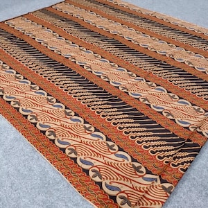 May include: A patterned textile with a repeating design of alternating stripes. The stripes feature intricate patterns in shades of brown, black, red, and beige. The fabric appears to be folded, with the pattern visible across the surface.