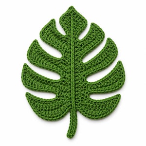 May include: A green crochet monstera leaf applique featuring a central stem and distinct cut-out sections along the edges. The textile piece is crafted with a visible yarn stitch pattern, creating a textured surface that mimics a natural plant leaf.