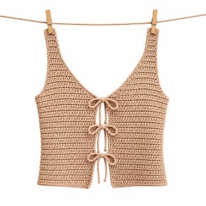 May include: A beige sleeveless crochet top featuring a deep V-neckline and a front opening secured by three matching tie closures. The garment is constructed with a horizontal ribbed stitch pattern and is suspended from a thin horizontal cord.