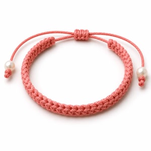 May include: A coral-colored braided cord bracelet featuring an adjustable sliding knot closure. The two loose ends of the cord are finished with small, round, white pearls secured by simple knots, creating a clean and symmetrical design.