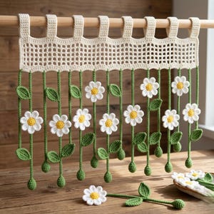 May include: Crocheted curtain with a cream-colored top section and hanging green stems with white and yellow daisy flowers. The curtain is suspended from a wooden rod. The daisies have yellow centers and white petals.
