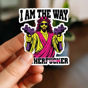 May include: A die-cut sticker featuring a graphic illustration of a bearded figure wearing a crown of thorns and sunglasses, holding two submachine guns. The text reads I AM THE WAY at the top and includes a partial word at the bottom with a bullet icon.
