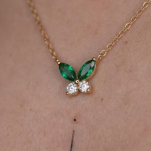 May include: A gold chain necklace featuring a butterfly-shaped pendant. The pendant is composed of two marquise-cut green gemstones forming the upper wings and two round-cut clear white gemstones forming the lower wings, set in gold metal.
