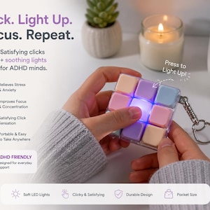 Op de afbeelding: Een handzame, veelkleurige kubus met zachte LED-verlichting, ontworpen voor ADHD-ondersteuning. De kubus heeft pastelkleurige vierkanten en een zilveren sleutelhanger. De tekst luidt: "Click. Light Up. Focus. Repeat."