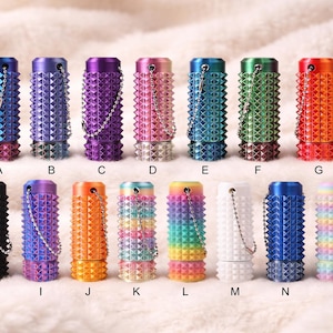 May include: A collection of colorful, cylindrical metal containers with a studded texture. Each container has a matching base and a small chain. The colors include blue, purple, pink, green, orange, and rainbow hues.