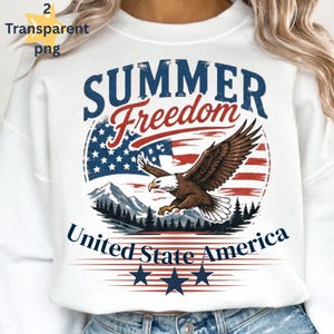 Könnte beinhalten: Ein weißes Sweatshirt mit einer Grafik, die einen Weißkopfseeadler zeigt, der über ein Gebirge und einen Wald fliegt. Das Design enthält den Text "SUMMER Freedom" und "United State America" vor einem stilisierten amerikanischen Flaggenhintergrund und drei marineblauen Sternen.