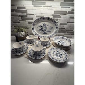 Op de afbeelding: Een complete blauw-witte porseleinen theeset. De set bevat een grote ovale schaal, theekopjes met schotels, kleine borden en een serveerschaal. Het bloemmotief wordt herhaald in de hele set, met een decoratieve rand.