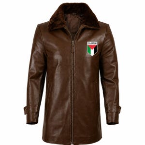 Puede incluir: Una chaqueta de cuero marrón con cuello de piel sintética marrón oscuro y cierre de cremallera central. El pecho muestra un pequeño parche en forma de escudo con la bandera de Palestina y el texto PALESTINE en letras mayúsculas negras.