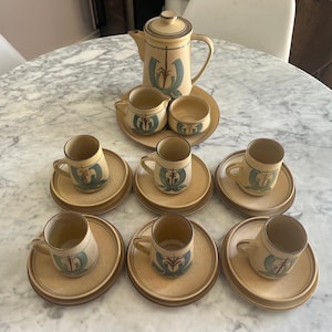 May include: A vintage beige ceramic coffee set, including a teapot, creamer, sugar bowl, and eight cups and saucers. Each piece has a teal and brown design. The set is displayed on a marble table.