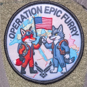 May include: A circular patch with the text "OPERATION EPIC FURRY" encircling a design. The design features a cartoon fox and wolf giving a high-five, with an American flag and a world map in the background. The patch is on a green fabric.
