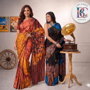 May include: Two batik sarees featuring intricate patterns. One saree displays warm orange, yellow, and deep red tones with a crackled texture. The other saree is black with blue and orange floral motifs, paired with a blue beaded necklace.