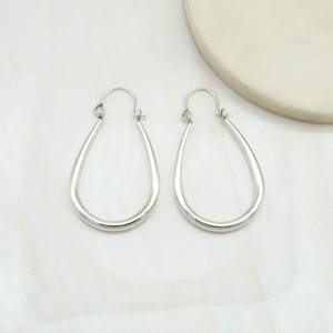 May include: A pair of silver-toned hoop earrings with a teardrop shape. Each earring features a smooth, polished metal finish and a hinged wire closure at the top, creating a continuous, rounded silhouette that tapers to a point at the base.