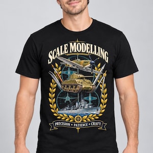 May include: A black short-sleeve t-shirt featuring a graphic print with the text SCALE MODELLING at the top and PRECISION PATIENCE CRAFT on a banner at the bottom. The design includes illustrations of a fighter plane, a tank, and a naval ship.