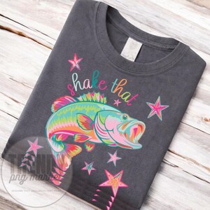 Pu&ograve; includere: T-shirt grigio scuro con un'illustrazione colorata di un pesce e la scritta "shake that". Il design include stelle di vari colori, creando un look divertente e vivace. Un capo di abbigliamento casual.