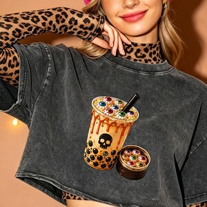May include: A charcoal grey acid-wash cropped t-shirt layered over a long-sleeve leopard print mock-neck top. The t-shirt features a graphic of a bubble tea cup filled with eyeballs and a skull icon, alongside a small bamboo steamer filled with eyeballs.