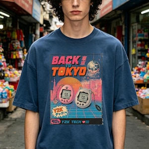 May include: A navy blue t-shirt featuring a graphic print with the text BACK TO TOKYO, a disco ball, a sunset cityscape, and two digital pet devices. One device is pink with a paw print, and the other is white with cat ears, both on a grid.