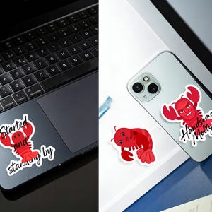 May include: A collection of red lobster stickers. One sticker features a lobster with the text "Started and stanning by". Another sticker shows a lobster with the text "Handsome Molly". The stickers are on a laptop and a phone.