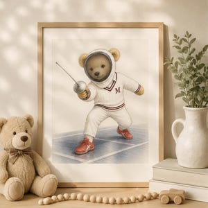 May include: A framed wall art print featuring a teddy bear dressed in a white fencing uniform with a maroon letter M on the chest. The bear wears a fencing mask and holds a foil, standing on a blue court while wearing red athletic shoes.