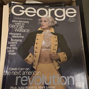 Może przedstawiać: Okładka magazynu "George". Na okładce widnieje osoba w żółto-czarnym stroju w stylu wojskowym. Tytuł magazynu jest dużymi białymi literami. Okładka zawiera również tekst o Johnie Kennedym, Madonnie i "następnej amerykańskiej rewolucji."