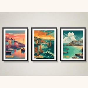 May include: Three framed art prints depicting coastal scenes. The prints feature colorful illustrations of Padstow, Falmouth, and St Ives, with boats, buildings, and water. Each print has a black frame and a cream-colored background.