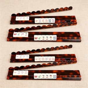 Pode incluir: Quatro suportes retangulares para pe&ccedil;as de Mahjong com padr&atilde;o de casco de tartaruga castanho e bordos superiores recortados. Cada suporte cont&eacute;m pe&ccedil;as brancas com desenhos florais coloridos e o texto WEN, WEI e JOKER impresso.