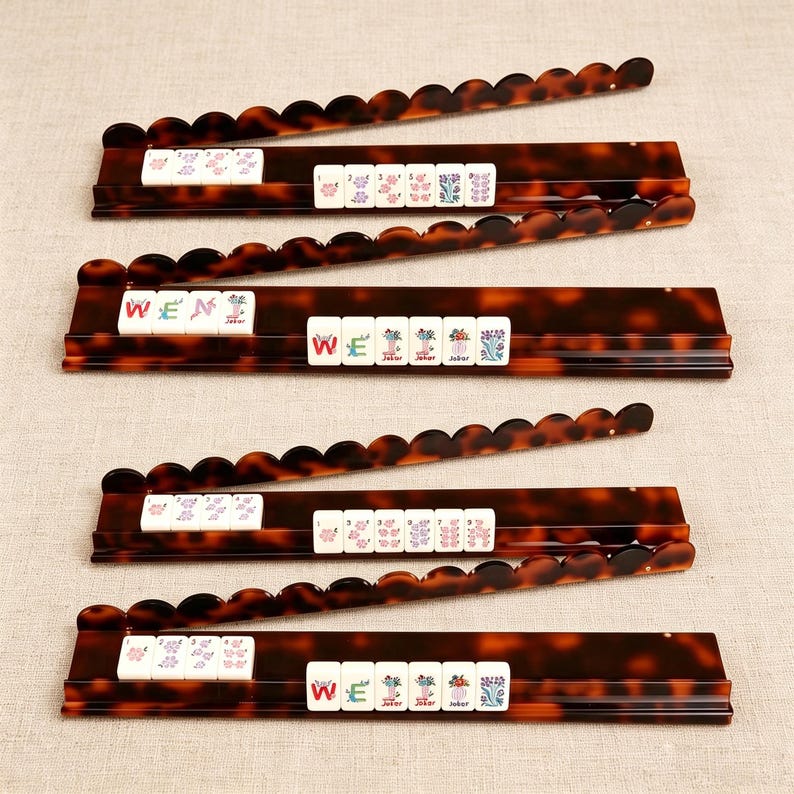 Pode incluir: Quatro suportes retangulares para pe&ccedil;as de Mahjong com padr&atilde;o de casco de tartaruga castanho e bordos superiores recortados. Cada suporte cont&eacute;m pe&ccedil;as brancas com desenhos florais coloridos e o texto WEN, WEI e JOKER impresso.