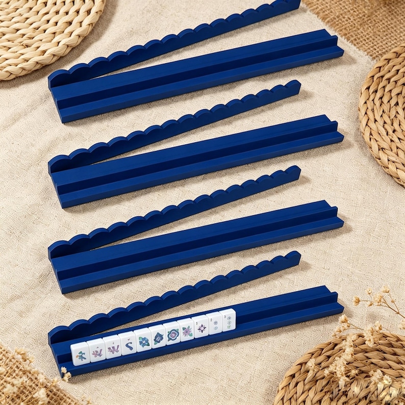 May include: Four dark blue wooden tile racks with a scalloped top edge and a grooved base for holding game pieces. The bottom rack contains ten white rectangular tiles with various colorful printed symbols and numbers arranged in a single row.
