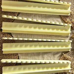 May include: A set of four pale yellow wall-mounted shelves, each featuring a scalloped front edge and a flat back panel with pre-drilled holes for mounting. The shelves have a smooth, matte finish and a narrow ledge for displaying small items.