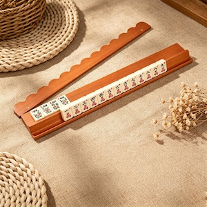 Pu&ograve; includere: Due lunghi supporti in legno per tessere del mahjong con bordo superiore smerlato. Un supporto contiene una fila di tredici tessere color bianco sporco con caratteri cinesi rossi e verdi e motivi floreali, disposte in ordine numerico da uno a nove.
