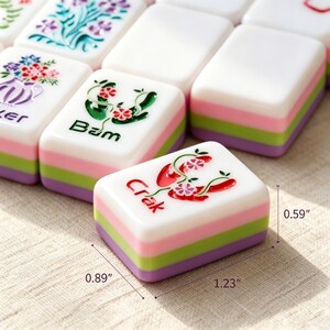 Pode incluir: Um conjunto de pe&ccedil;as retangulares de Mahjong com uma camada superior branca apresentando gravuras florais e bot&acirc;nicas coloridas, incluindo o texto 'Bam' e 'Crak'. Cada pe&ccedil;a tem lados em camadas rosa, verde e roxo, medindo 3,12 cm por 2,26 cm por 1,50 cm.