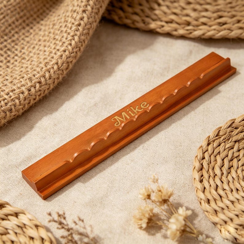 May include: A long, rectangular wooden display stand with a smooth, polished finish. The top edge features a series of rounded, scalloped cutouts along its length. The name Mike is engraved in a cursive script font on the front face of the wood.