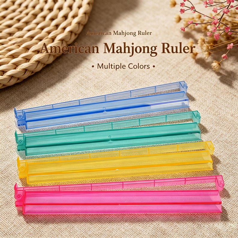 May include: Four translucent plastic American Mahjong rulers in blue, teal, yellow, and pink. Each ruler features a hinged design with a central groove and a small circular pivot point on the left side. The text American Mahjong Ruler is visible.